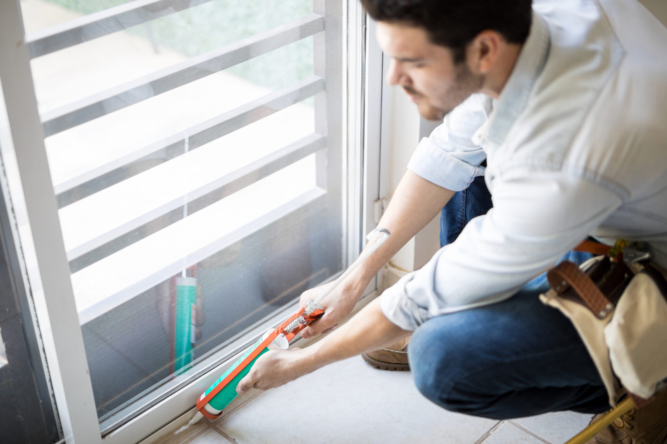 closeup young handyman applying some sealant door with sealing gun scaled